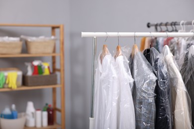 Dry-cleaning service. Hangers with different clothes in plastic bags on rack indoors, space for text