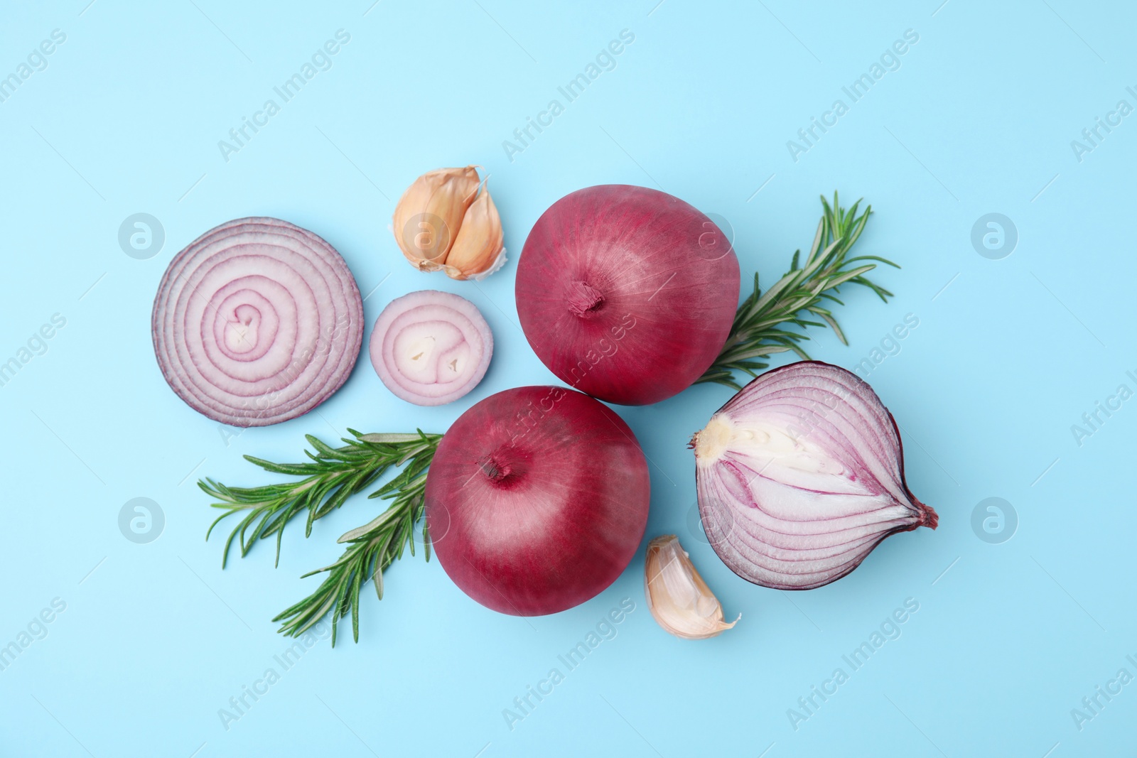 Photo of Fresh red onions, garlic and rosemary on light blue background, flat lay