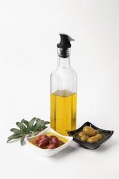 Bottle of cooking oil, olives and leaves on white background