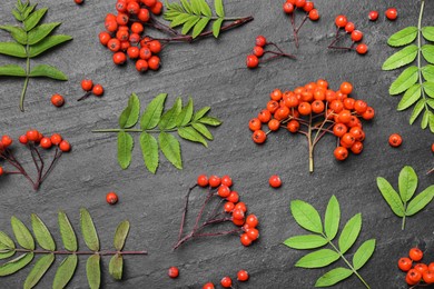 Photo of Fresh ripe rowan berries and green leaves on black table, flat lay