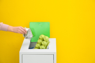 Woman putting used foil container into trash bin on color background, closeup with space for text. Recycling concept