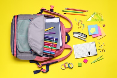 Flat lay composition with backpack and school stationery on yellow background