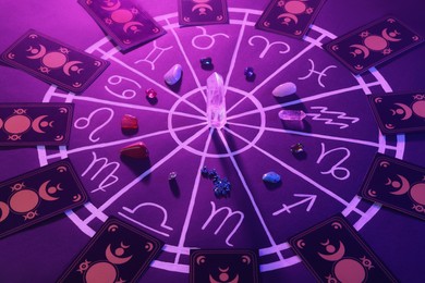 Photo of Natural stones for zodiac signs, tarot cards and drawn astrology chart on purple background. Color tone effect