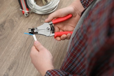Photo of Professional electrician stripping wiring at wooden table, above view