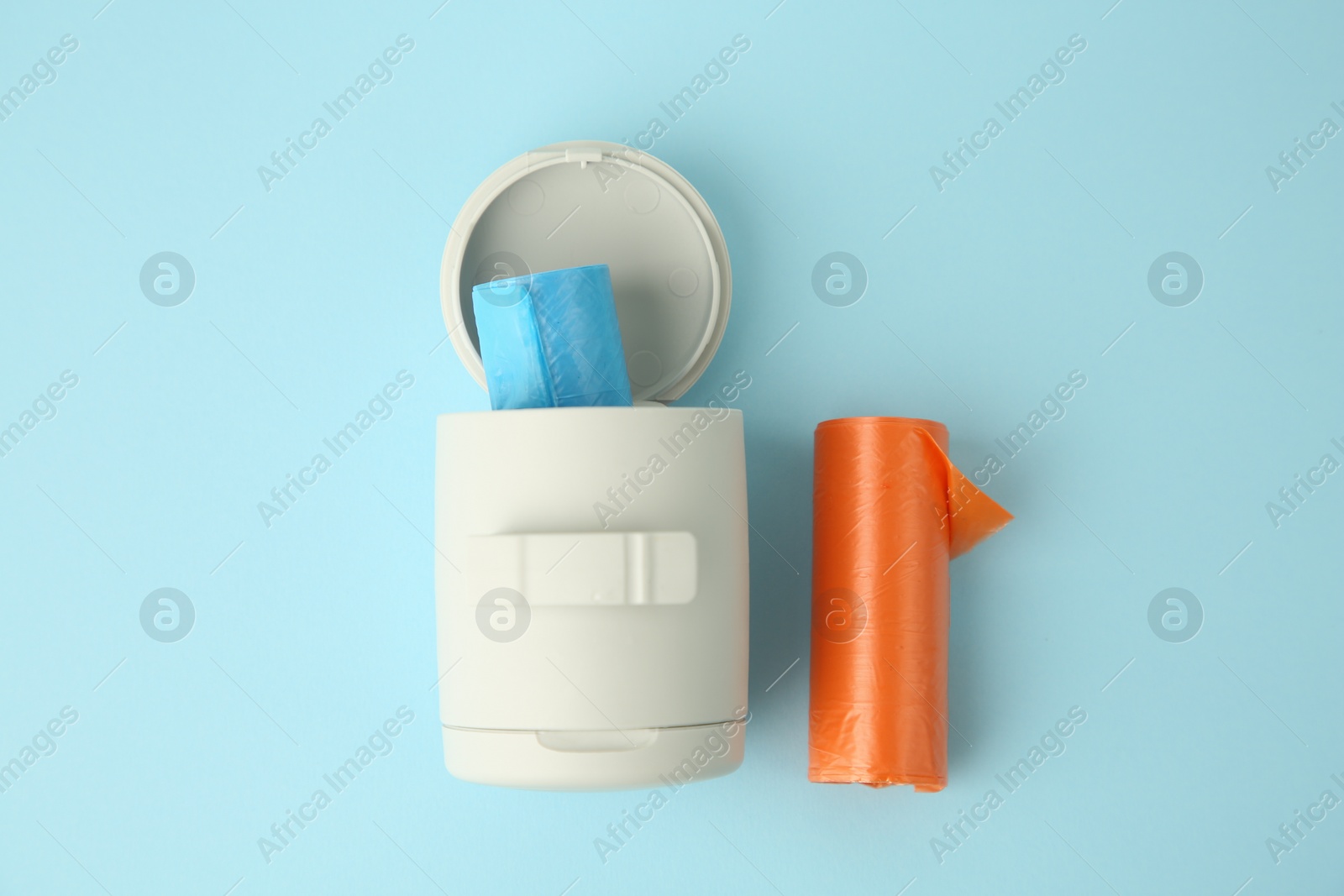 Photo of Dog waste bags and dispenser on light blue background, flat lay