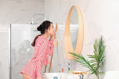Photo of Young woman brushing teeth near mirror in bathroom
