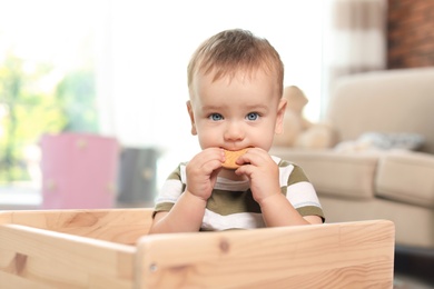 Photo of Adorable little baby eating tasty cookie indoors