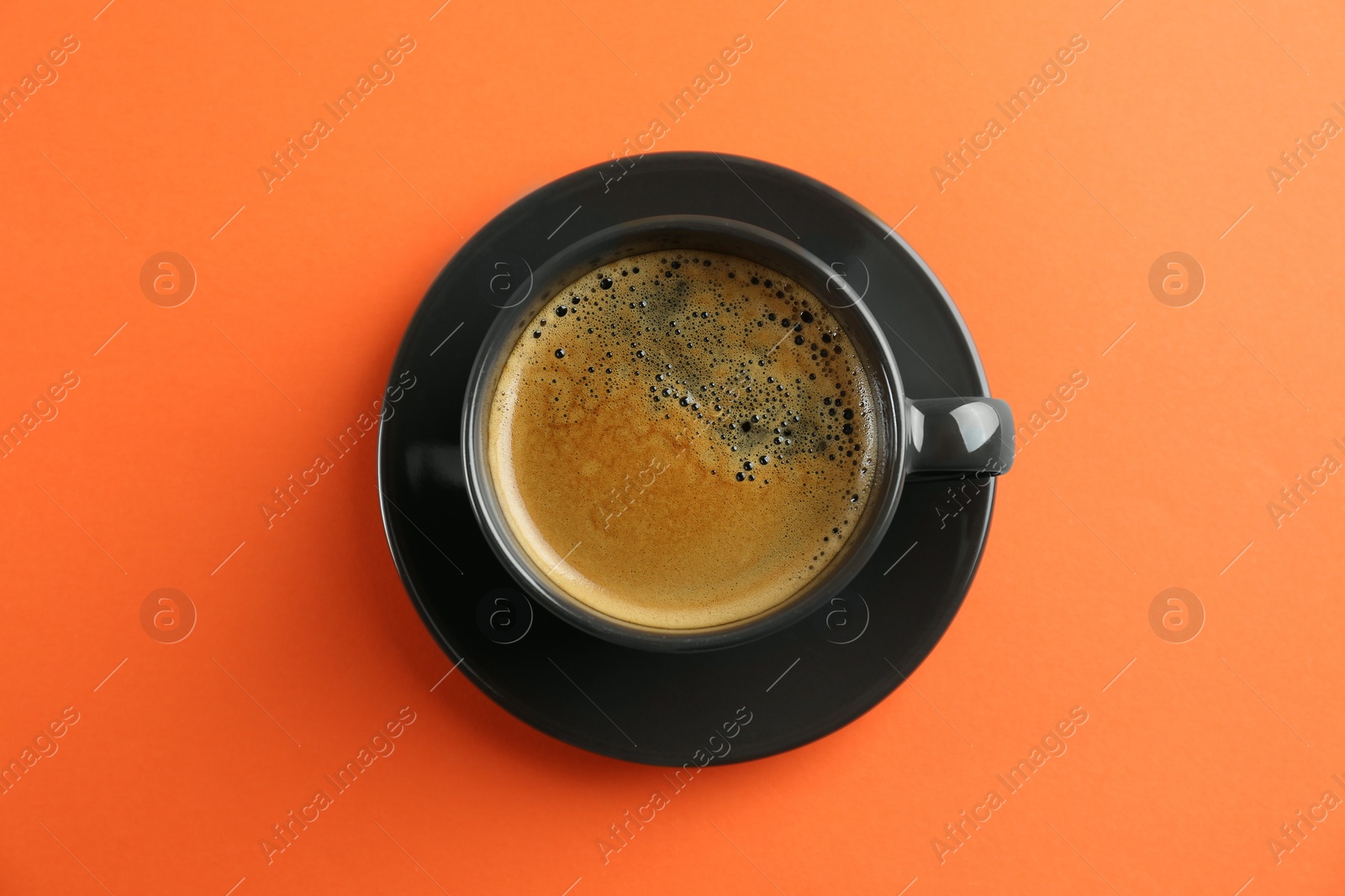 Photo of Cup of tasty coffee on orange background, top view