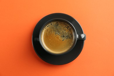 Cup of tasty coffee on orange background, top view