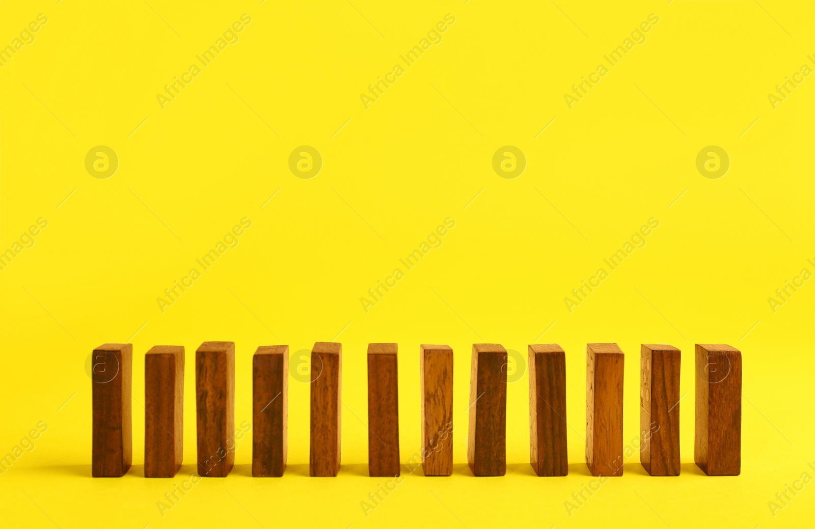 Photo of Row of wooden domino tiles on yellow background. Space for text