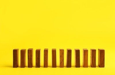 Row of wooden domino tiles on yellow background. Space for text