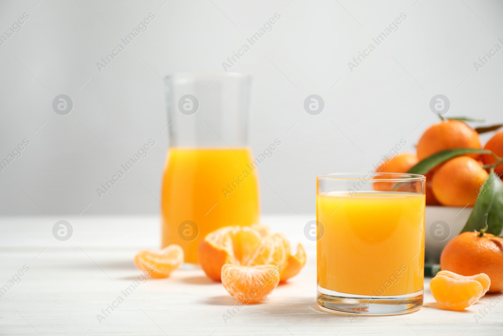 Photo of Glass of fresh tangerine juice and fruits on white wooden table. Space for text