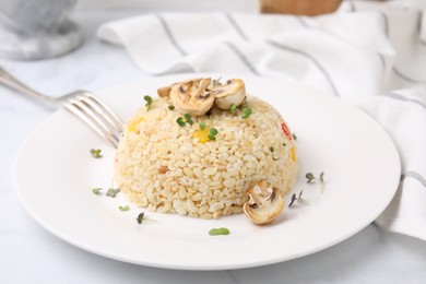 Photo of Delicious bulgur with vegetables, mushrooms and microgreens served on table, closeup