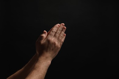Photo of Religion. Christian man praying on black background, closeup. Space for text