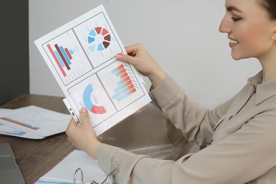 Photo of Businesswoman working with charts at wooden table in office, closeup