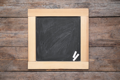 Photo of Blackboard with pieces of chalk on wooden background, top view. Space for text