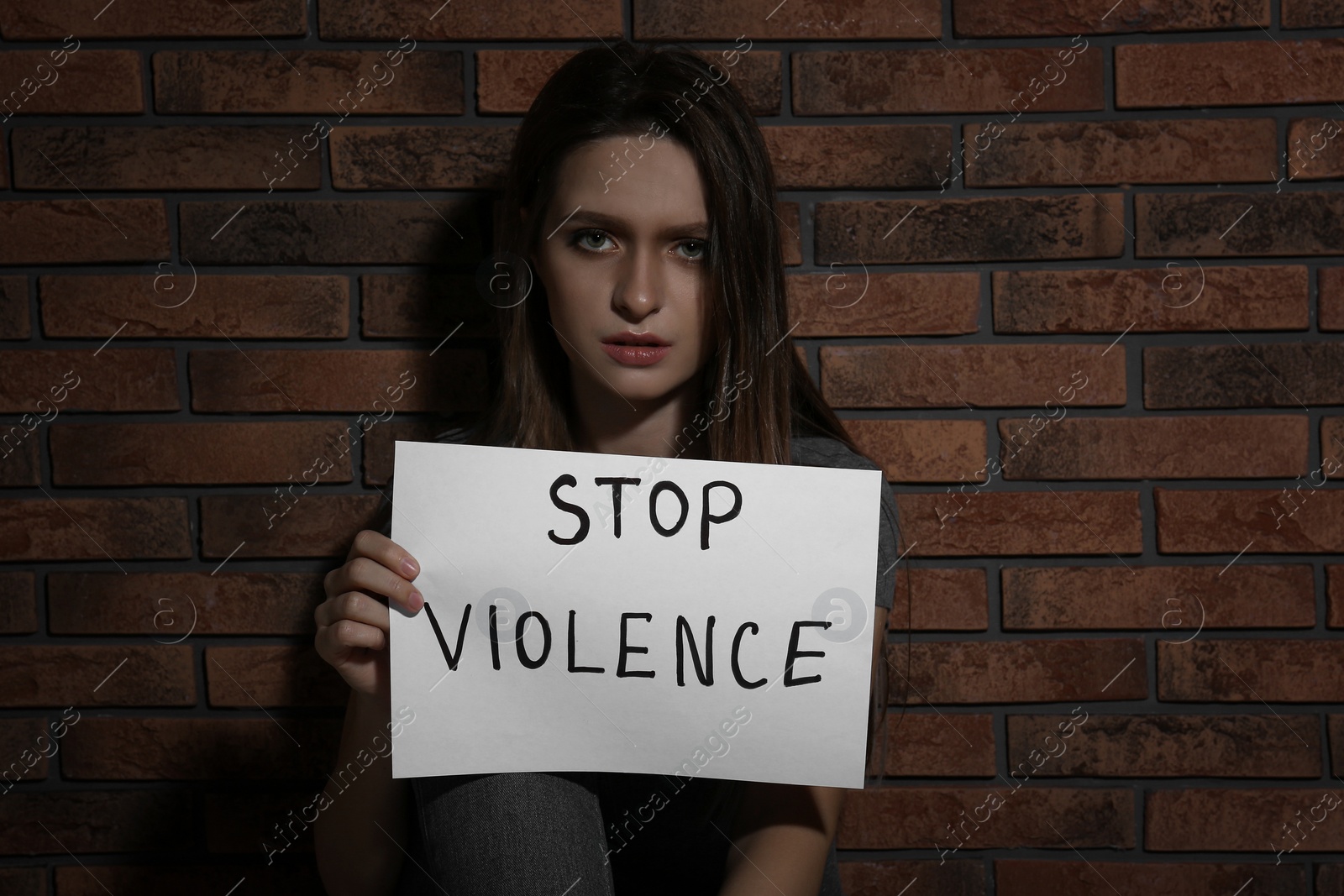 Photo of Abused young woman with sign STOP VIOLENCE near brick wall