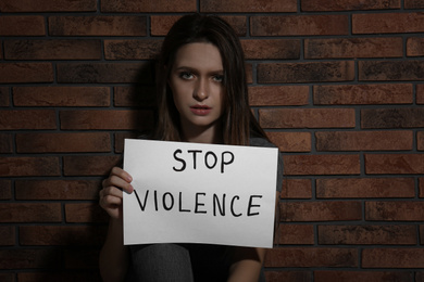 Abused young woman with sign STOP VIOLENCE near brick wall