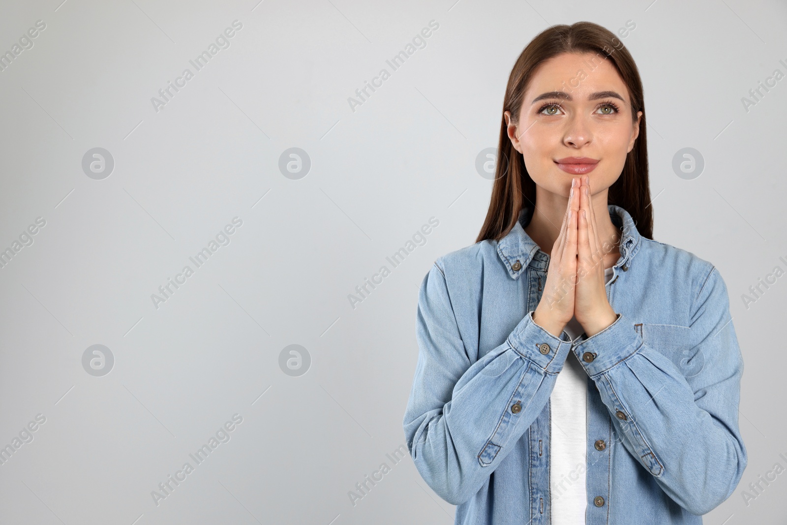 Photo of Woman with clasped hands praying on light grey background, space for text