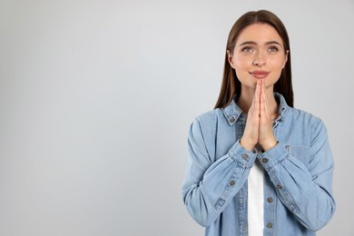 Woman with clasped hands praying on light grey background, space for text