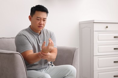 Asian man suffering from pain in his hand on armchair indoors
