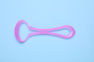 Photo of Pink tongue cleaner on light blue background, top view