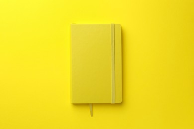 Photo of Closed notebook on yellow background, top view