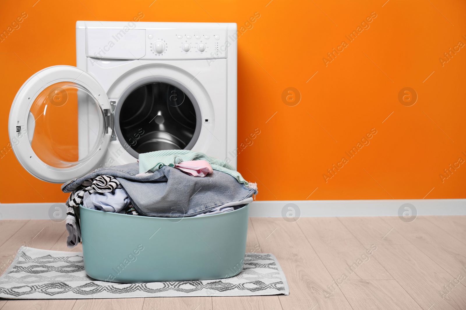 Photo of Laundry basket with clothes on floor near washing machine in bathroom. Space for text