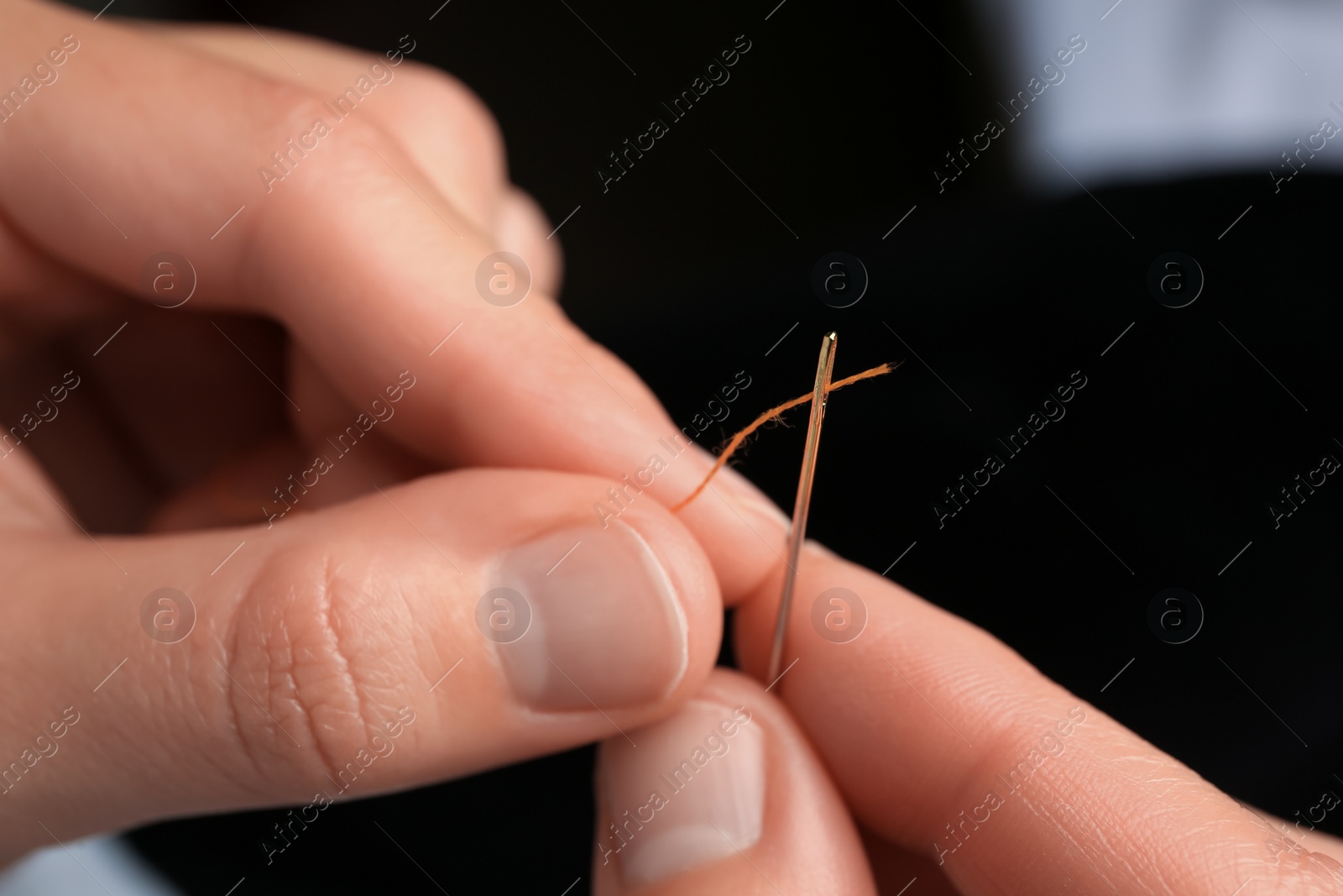 Photo of Woman threading sewing needle on blurred background, closeup