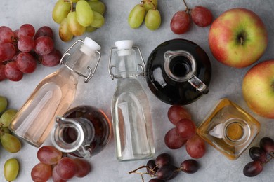 Photo of Different types of vinegar and fresh fruits on grey table, flat lay