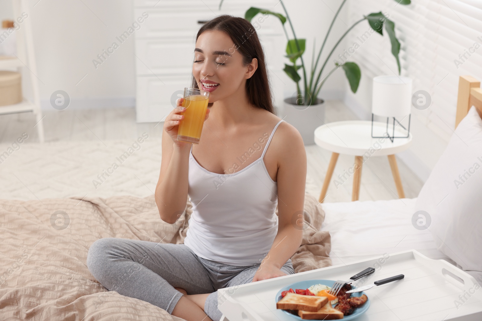 Photo of Happy young woman having breakfast on bed at home