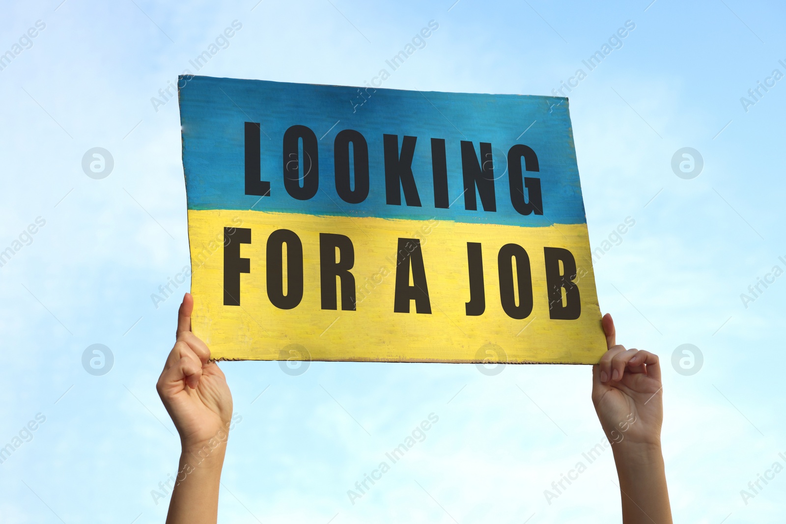 Image of Unemployed due to war. Woman holding poster in colors of Ukrainian flag and phrase Looking For A Job against sky, closeup