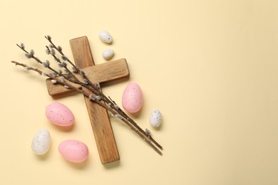 Wooden cross, painted Easter eggs and willow branches on beige background, flat lay. Space for text