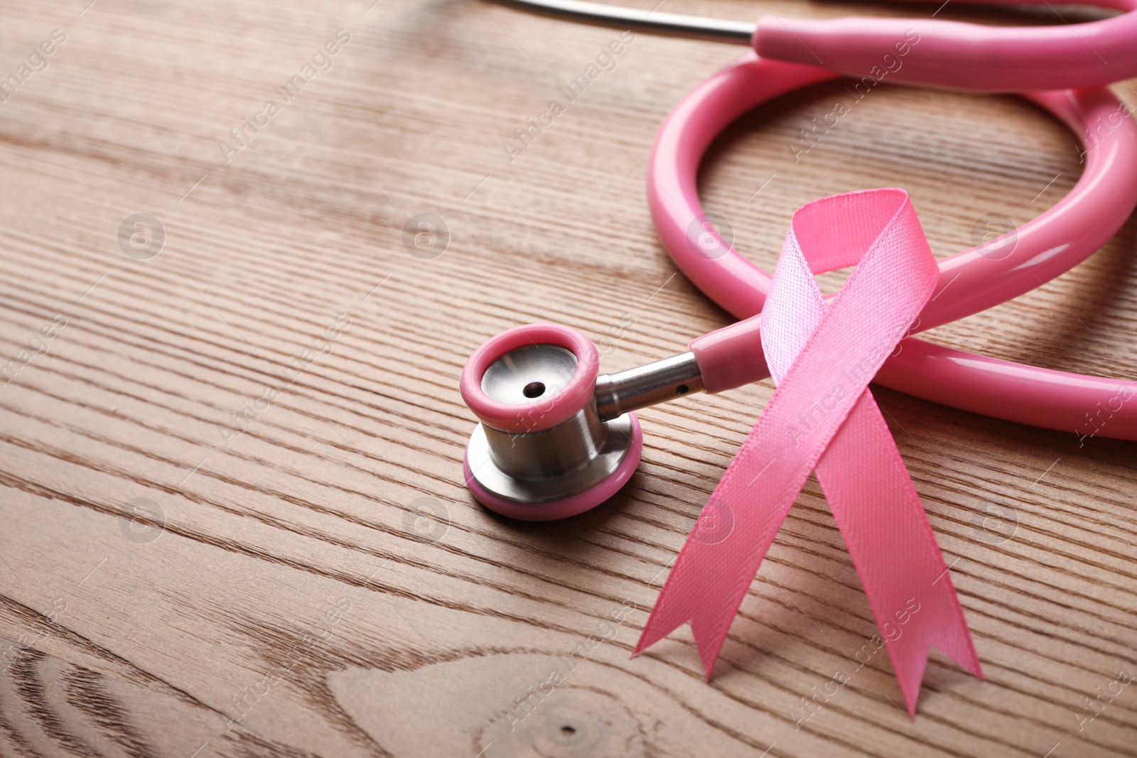 Photo of Pink ribbon and stethoscope on wooden background, space for text. Breast cancer concept