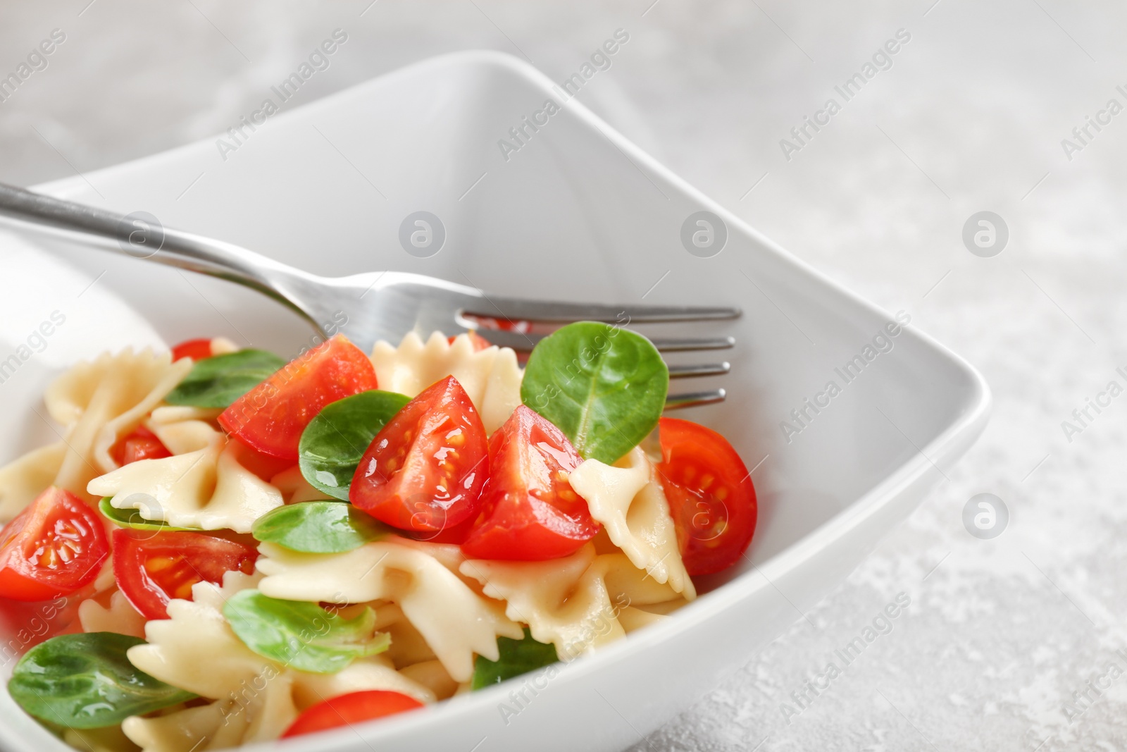 Photo of Bowl with delicious pasta primavera on grey background