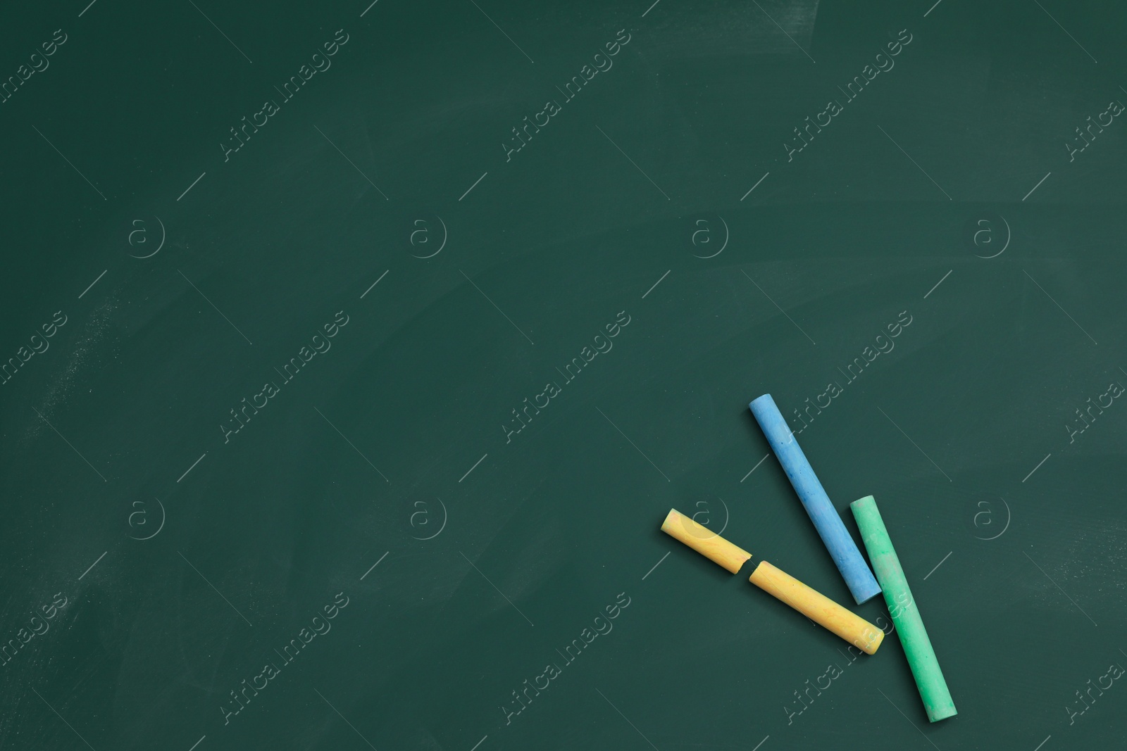 Photo of Colorful chalks on green board, flat lay. Space for text