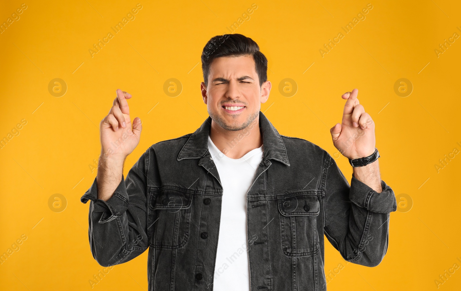 Photo of Man with crossed fingers on yellow background. Superstition concept