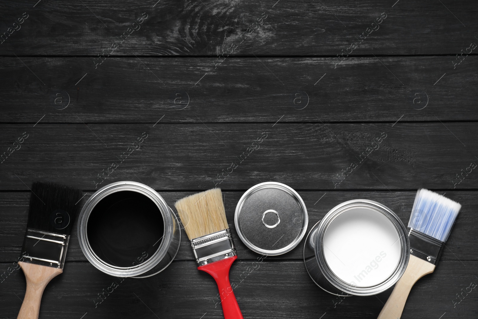 Photo of Cans of white and black paints with brushes on wooden table, flat lay. Space for text