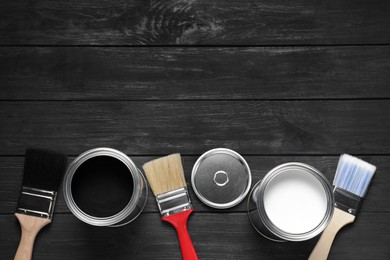 Photo of Cans of white and black paints with brushes on wooden table, flat lay. Space for text