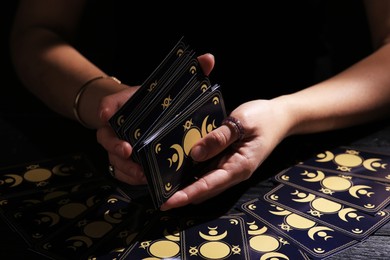 Soothsayer shuffling tarot cards at table in darkness. Fortune telling