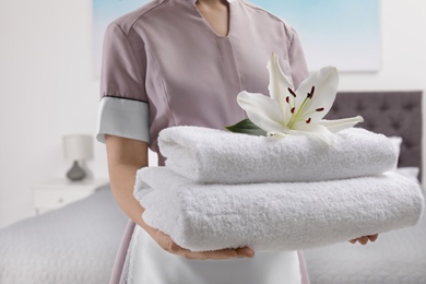 Maid holding fresh towels with flower in hotel room, closeup
