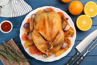 Photo of Roasted chicken with oranges on blue wooden table, flat lay