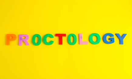 Photo of Word PROCTOLOGY made of colorful letters on yellow background, top view. Hemorrhoid problems