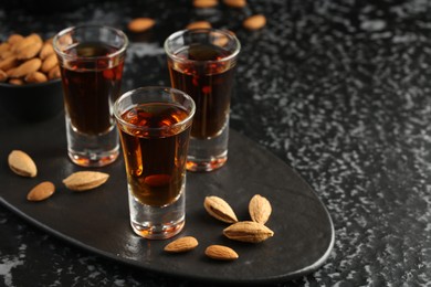 Glasses with tasty amaretto liqueur and almonds served on black table, closeup. Space for text