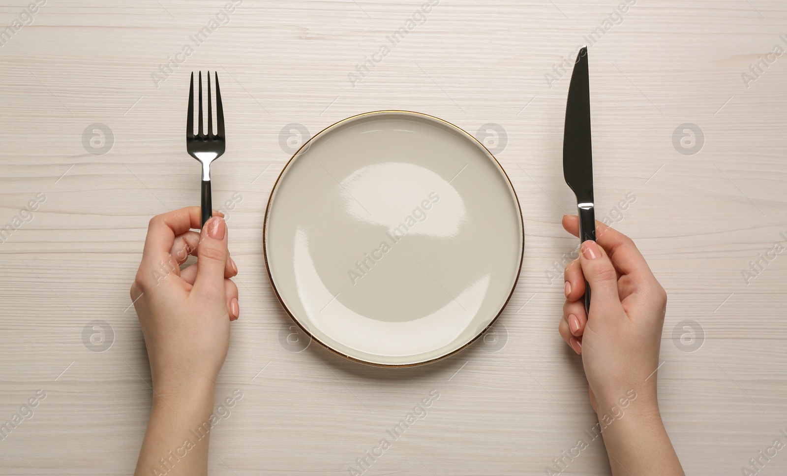 Photo of Woman with empty plate and cutlery at white wooden table, top view