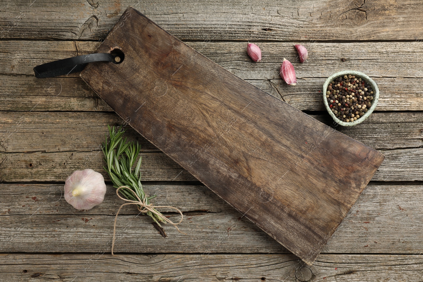 Photo of Cutting board, garlic, pepper and rosemary on wooden table, flat lay. Space for text