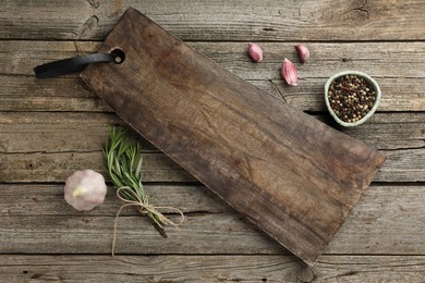 Photo of Cutting board, garlic, pepper and rosemary on wooden table, flat lay. Space for text