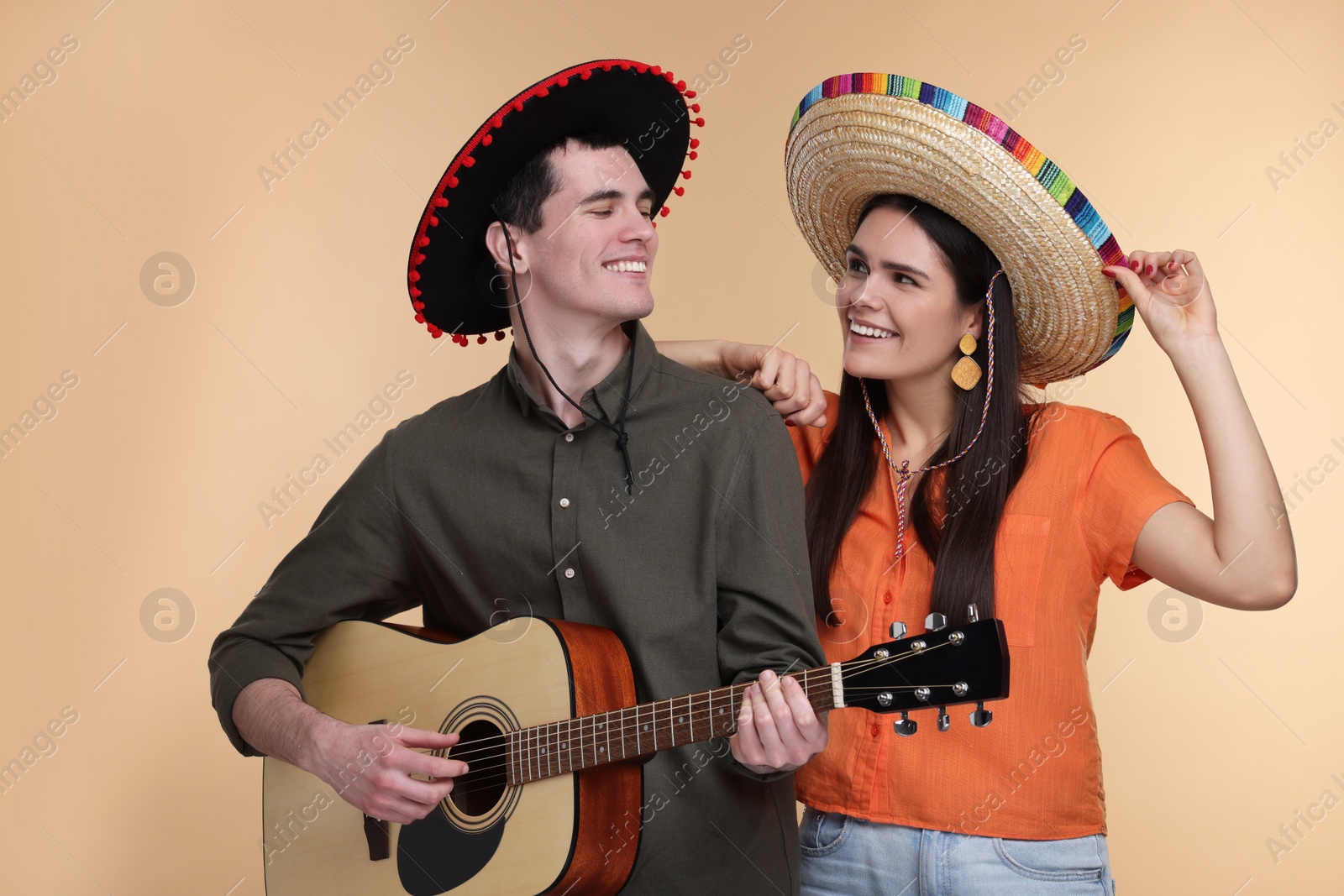 Photo of Lovely couple woman in Mexican sombrero hats playing guitar on beige background