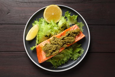 Photo of Delicious cooked salmon with pesto sauce, lettuce and lemon on wooden table, top view