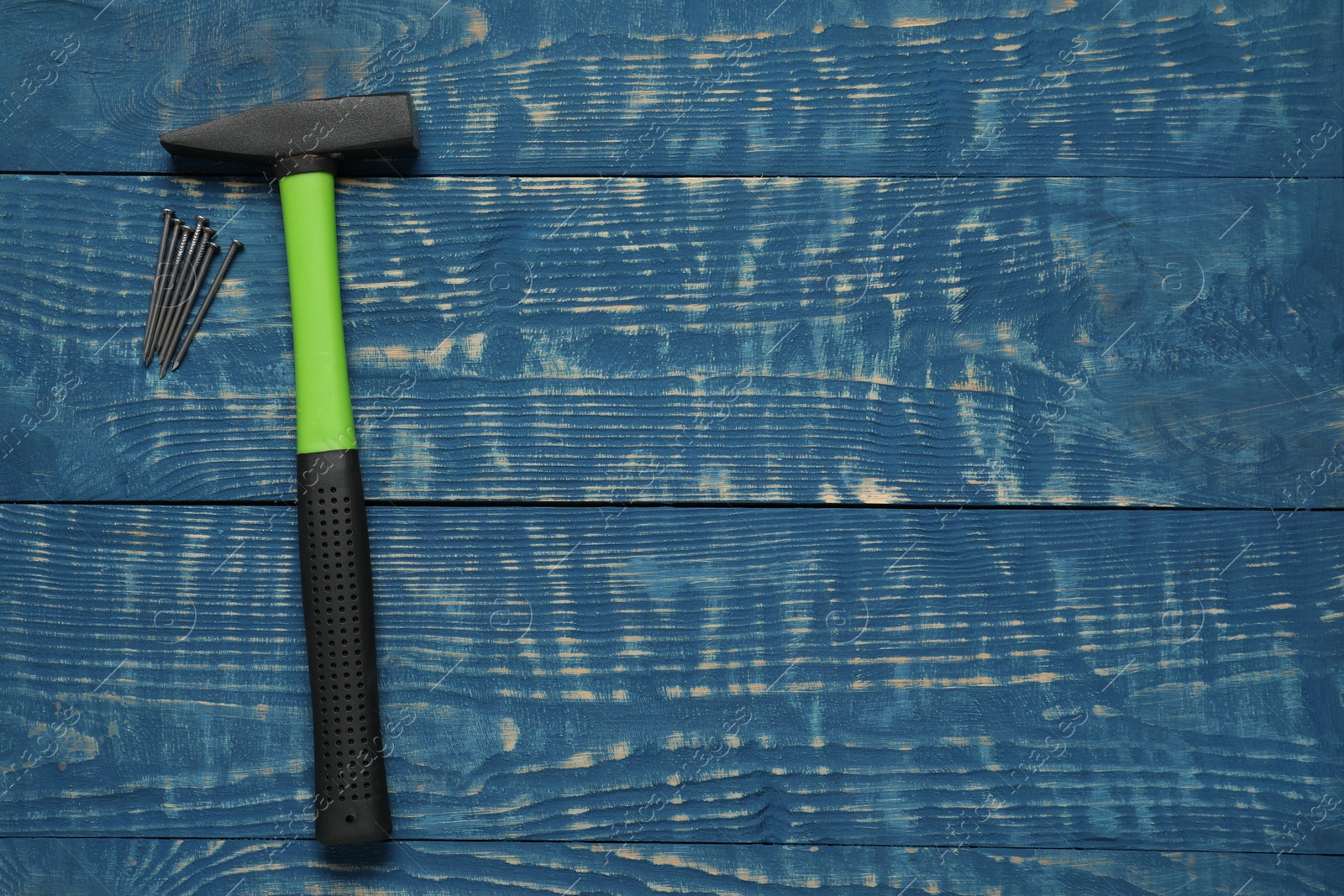 Photo of New hammer and metal nails on blue wooden table, flat lay. Space for text